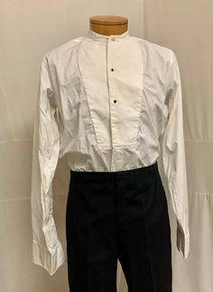 "1900, 15 1/4\" Neck, white cotton collarless shirt with pique bib front, 3 button holes for studs.  Shirt opens to hem in front, and buttons down at back 3/4 way. Curved at each hip at bottom.  Sleeves are long with  double French cuffs. Label reads \" Simpson Piccadilly. Measurements: neck 15 1/4\" Chest 42\" Shoulder to shoulder 16\" Shoulder to hem 30\" Sleeves 25\" Arm holes 9\" Width at bottom 44\"" Classic Cotton Shirt With Stand Collar, White Formal Shirt With Stand Collar, Formal White Shirt With Stand Collar, Classic White Shirt With Stand Collar, Classic Shirt With Stand Collar And Buttons, White Shirt With Covered Buttons For Daywear, White Dress Shirt For Daywear, Collarless Shirt, French Cuff