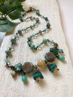 This bohemian style floral necklace was created from a bounty of aqua and turquoise beads. The flower cluster in the front features all Czech glass beads - teardrops, bicones, hibiscus flowers, maple leaves, melons and bell flowers. The sides are made up of alternating stations of iridescent pale aqua glass rounds and graduated genuine turquoise gemstone rondelles linked together by vintage finish brass wire. This necklace closes with a brass lobster claw clasp with even more itty bitty czech Czech Beads Jewelry, Bell Flowers, Czech Glass Necklace, Czech Glass Jewelry, Pale Aqua, Flower Cluster, Aqua Glass, Art Necklaces, Necklace Flower