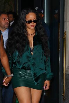 a woman with long black hair wearing a green shirt and leather skirt is walking down the street