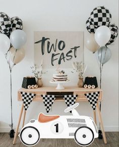 a race car birthday party table with balloons and streamers on the wall, including a sign that says two fast