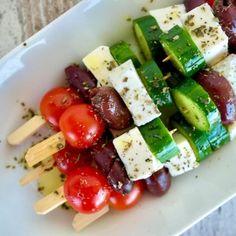 a white plate topped with cucumbers, tomatoes and other veggies on skewers