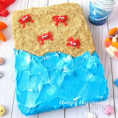 there is a cake with blue icing and red crabs on the beach in the sand