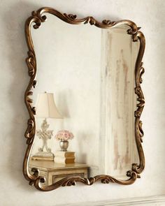 an ornate gold framed mirror sitting on top of a mantle next to a table with a lamp