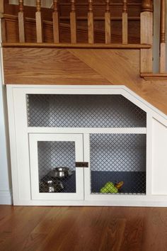 a dog house under the stairs with its doors open and food in it's bins