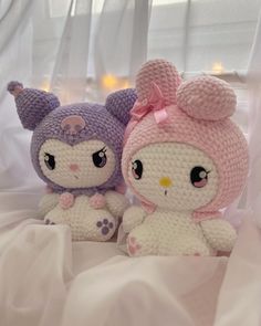 two crocheted stuffed animals sitting next to each other on a white bed sheet