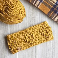 a yellow knitted headband next to a brown and blue plaid scarf on a white wooden surface