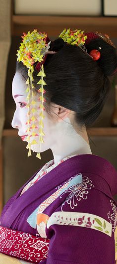 a geisha woman with flowers in her hair wearing a purple kimono and looking off to the side