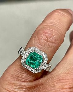 a close up of a person's hand holding a ring with a green stone