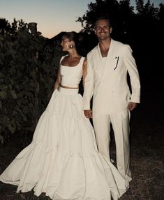 a man and woman dressed in white standing next to each other on grass covered ground