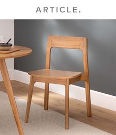 a wooden chair sitting next to a table on top of a carpeted floor in front of a gray wall