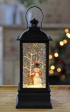 a snowman is in the center of a lighted lantern on a table next to a christmas tree