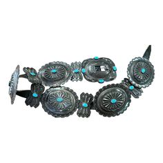 This old Navajo Concho belt with its cross hallmark on the buckle is the work of Navajo silversmith Etsitty Tsosie.  Set with turquoise throughout and strung on a buffalo hide strap.  Strap measures 40.5" long.  Buckle measures 4" x 3 1/4".  Round conchos measure 3 3/4" x 3 1/4".  Good condition with pleasing old surface. Southwestern Turquoise Concho Belt Buckles, Western Turquoise Belt With Concho, Turquoise Western Belt With Concho, Traditional Silver Concho Belt, Adjustable Southwestern Concho Belt Buckles, Silver Southwestern Concho Belt, Southwestern Silver Concho Belt, Southwestern Turquoise Jewelry With Antique Buckle, Adjustable Southwestern Silver Belt