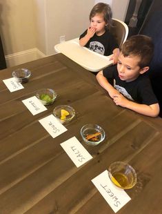 two young boys sitting at a table with food on it and paper signs in front of them