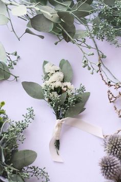 flowers and greenery laid out on a white surface with a ribbon tied around them