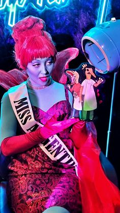 a woman with red hair and makeup sitting in a chair next to a neon sign