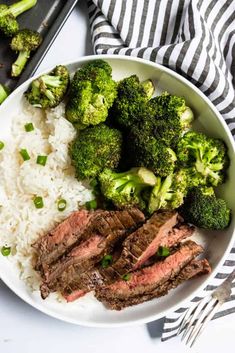 a white plate topped with steak, broccoli and rice next to a fork