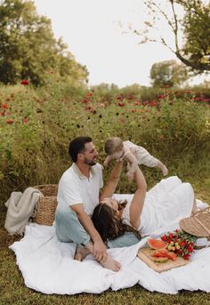 a man, woman and child are sitting on a blanket in the grass with flowers