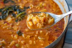 a spoon full of soup with broccoli and other food items in the bowl