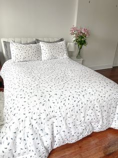 a bed with white sheets and pillows on top of wooden floor next to a flower vase