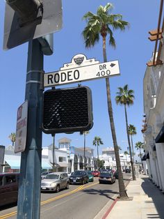 a street sign that reads rodeo dr in front of some palm trees and parked cars