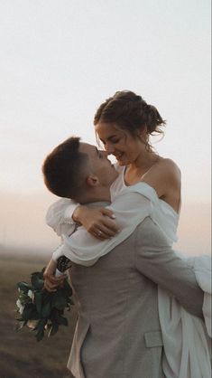 a bride and groom embracing each other on the beach at sunset in their wedding attire