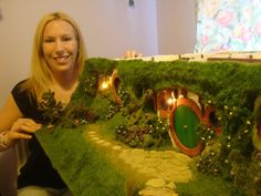 a woman sitting in front of a fake hobbot house made out of grass