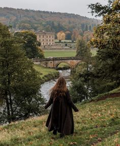 a woman walking down a hill next to a river