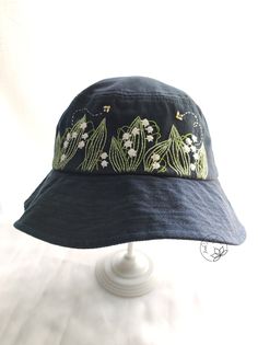 a blue hat with white flowers on the front and green leaves on the back, sitting on top of a table