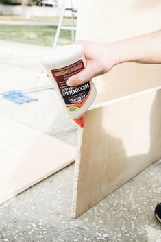 a person holding a bottle of wood glue near a piece of plywood planks