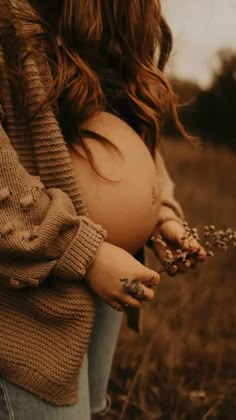 a pregnant woman standing in a field with her hands on her belly and holding flowers