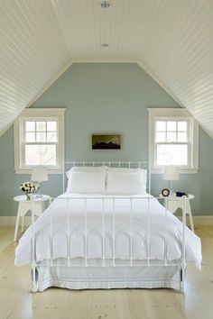 a white bed sitting under two windows in a bedroom