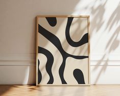 an abstract black and white painting on the wall next to a wooden floor with a plant