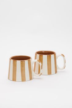 two coffee mugs sitting next to each other on a white surface with brown and white stripes