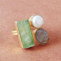 We always love using stones to create a color palette that helps us make versatile, chic pieces. For this design, we have used pale green natural kyanite, a light gray labradorite, and white luminescent pearl. The pastel palette exudes calm elegance with its simple metal detailing. It is a wonderful gift for your wife or a loved one. Product Details Item Code: BJBR-1380 Stone Name: Labradorite, Green Kyanite, Pearl Stone Shape : Round & Rectangle  Stone Size : 10*12mm, 10*22mm, & 8mm Metal: 18K Handmade Elegant Green Moonstone Ring, Unique Green Moonstone Ring For Anniversary, Elegant Handmade Green Moonstone Ring, Handmade Green Emerald Ring, Nature-inspired, Unique Green Rings With Natural Stones, Green Handmade Fusion Rings, Artisan Green Rings For Jewelry Making, Black Tourmaline Ring, Green Kyanite