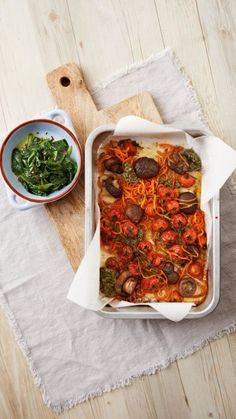 a casserole dish with mushrooms and carrots in it next to a bowl of greens