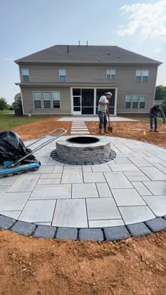 two men working on an outdoor fire pit in the middle of a yard that is being built