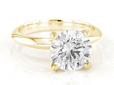 a yellow gold engagement ring with a round cut diamond in the center, on a white background