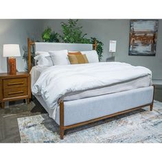 a white bed sitting on top of a rug next to a wooden dresser and lamp