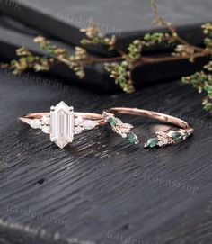 an emerald and diamond ring sitting on top of a wooden table next to some branches