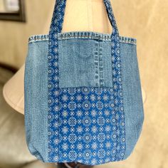 a denim bag with blue and white designs on the front, hanging from a mannequin's torso