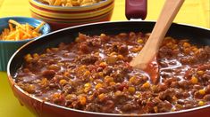 a red pot filled with chili and corn next to bowls of cheesy fries