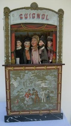 a group of dolls sitting on top of a wooden shelf in front of a painting