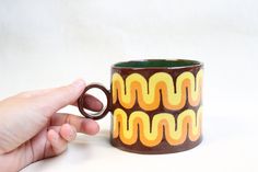 a hand holding a brown and yellow coffee mug with an abstract design on it's side