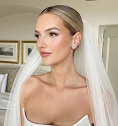 a woman wearing a wedding veil and diamond earrings is looking at the camera while standing in front of a bed