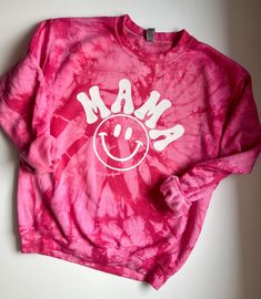 a pink tie - dye shirt with the word mam on it and a smiley face drawn in white