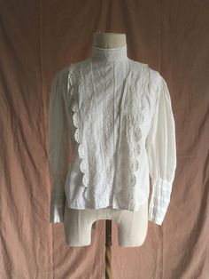 "vintage early 1900s antique true vintage blouse white cotton embroidered cotton lace mother of pearl buttons (except bottom button which is something else, maybe plastic) eyelet detail lace trim right of center buttons up front hidden under lace flap the button placement makes this seem to be originally meant for breast feeding  tie back hook eye back neck mutton chop sleeves front hem is longer than back hem good vintage condition  considering age w/signs of wear mended holes, fray, light tea/rust color stains here and there the buttons had wear around them enough for me to put patches under the buttons for re-enforcement all the buttons don't match but are of the era patches around back tie area patches around neck area repairs by me wearable measures, lying flat, shoulder-15 1/2\" ches Victorian Cotton Fitted Blouse, Fitted Victorian Cotton Blouse, Victorian White Cotton Top, Victorian Style White Cotton Top, Cotton Tops With Lace Trim For Weddings, Victorian Cotton Tops With Lace Trim, Victorian Cotton Blouse With Lace Collar, Victorian Cotton Top With Lace Trim, Vintage Fitted Tops With Broderie Anglaise