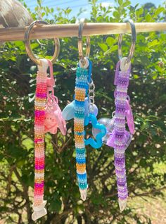 three key chains hanging from a tree branch with beads and charms attached to the ends