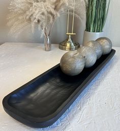 three silver balls on a black tray next to a vase with some grass in it