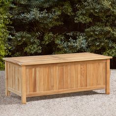 a wooden box sitting on top of a cement ground next to some bushes and trees