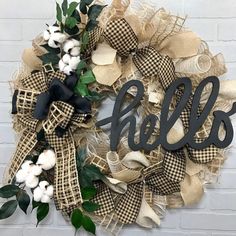 a wreath with the word hello is hanging on a brick wall next to cotton and greenery